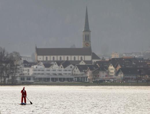 A man dressed as Santa Claus on a stand-up paddle crosses Lake Aegerisee near Unteraegeri, Switzerland December 5, 2015. REUTERS/Arnd Wiegmann