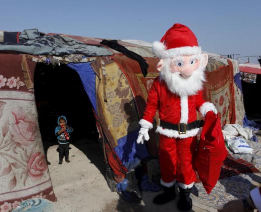A volunteer wearing a Santa Claus costume distributes presents to children at a poor community in Najaf, south of Baghdad, December 19, 2015.  REUTERS/Alaa Al-Marjani